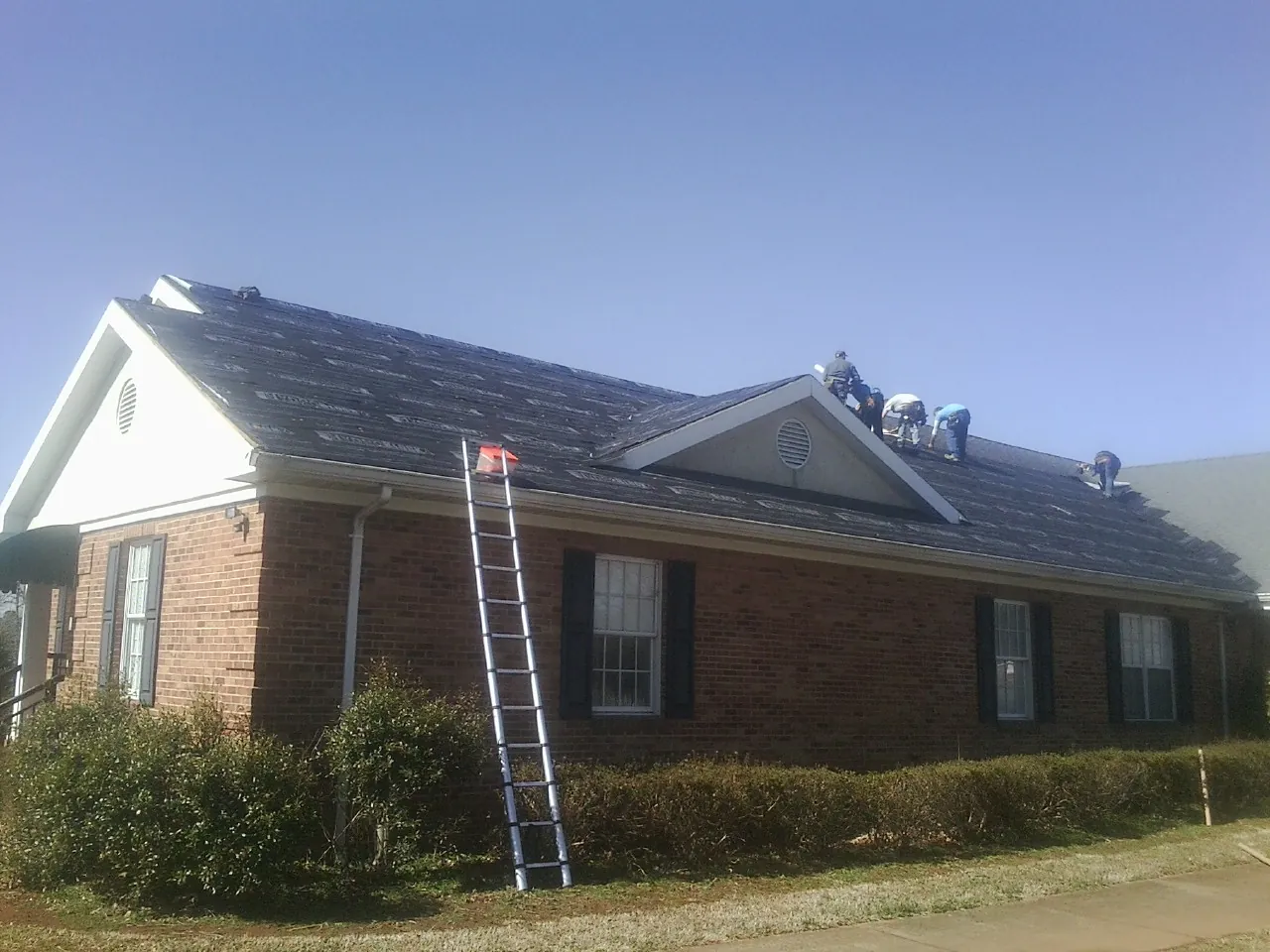 Crew tearing shingles off a brick ranch roof with a ladder set — Emergency Roof Repair work by our crew in Perry Point