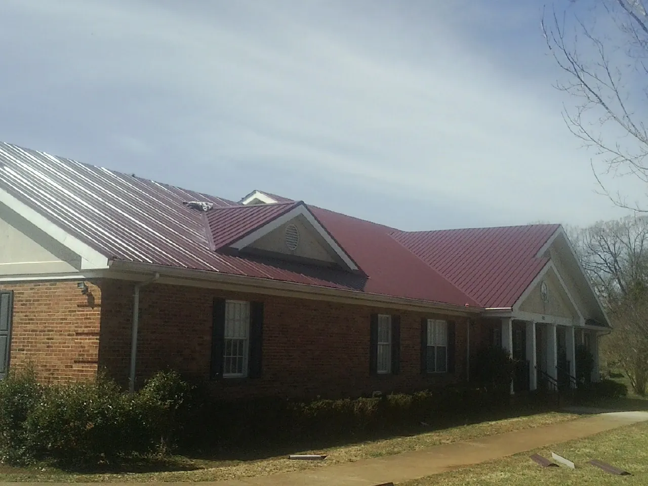 Red metal roof with gabled entries on a long brick building, from a Hail Damage Roof Repair job in Perry Point