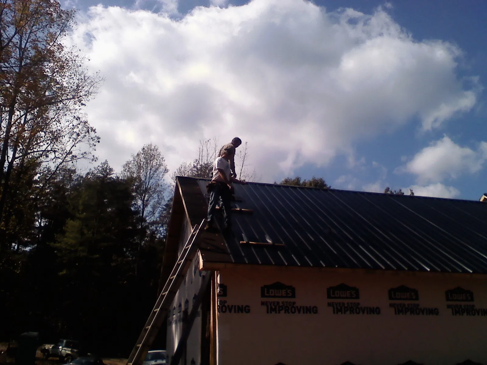 Roofer fastening dark metal panels high against a cloudy sky, from a Roof Inspection job in Perry Point