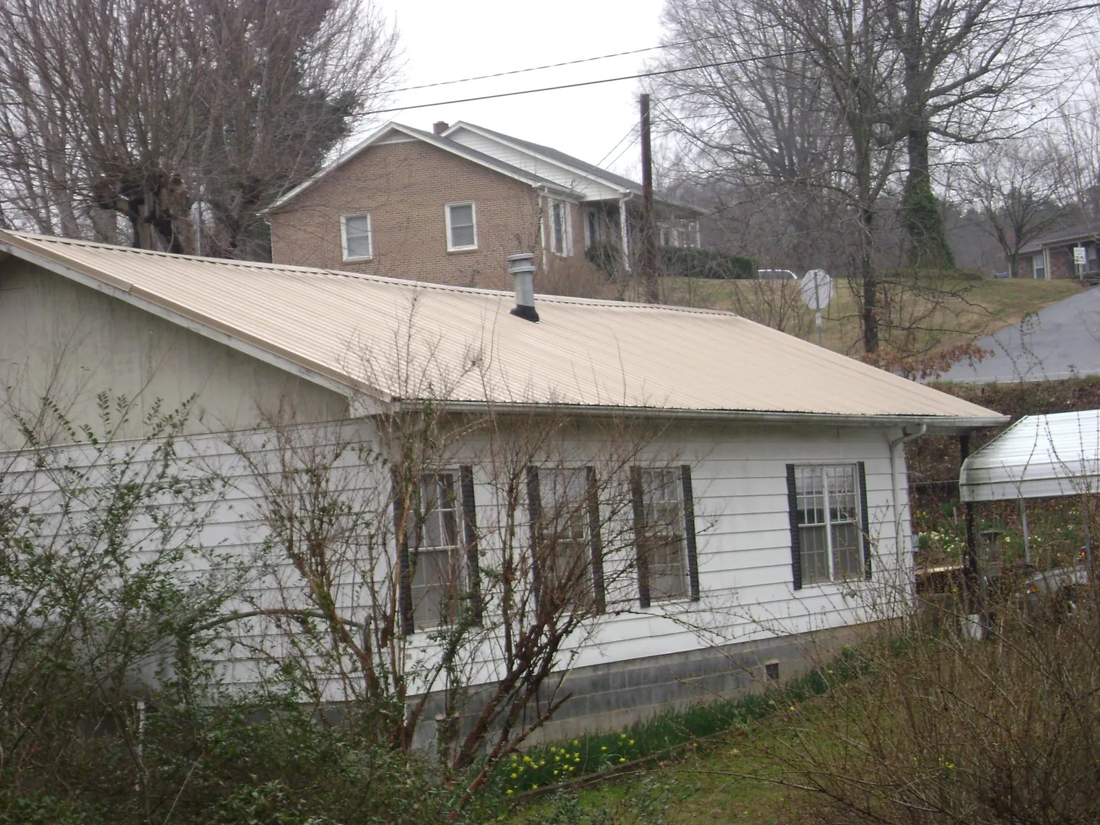 Tan metal roof on a white sided house set into a hillside — Commercial Roofing by Roofing Brothers in Perry Point