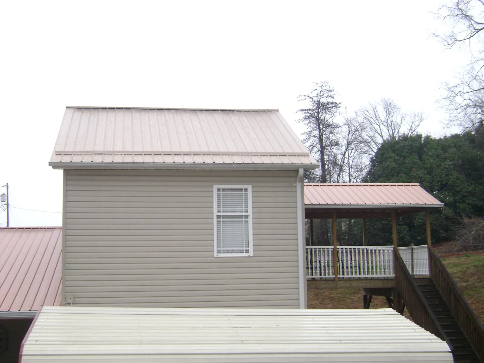 Tan metal roofs on a two story addition and attached porch, from a Roof Replacement job in Perry Point
